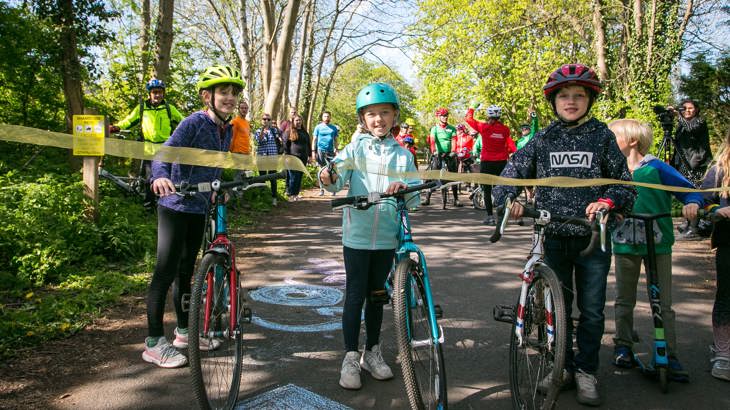 Wylam Waggonway launch event - Image of children with bikes cutting ribbon - spring day - sunny in a crowd under trees