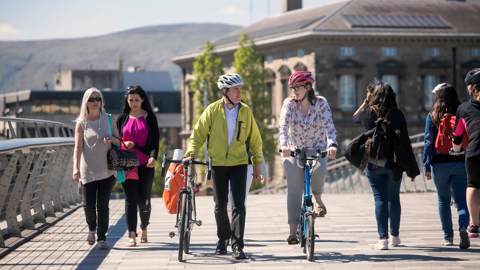 People walking and on bikes crossing bridge in urban setting