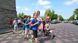 Children walking across a road while a woman pushes a buggy in the background