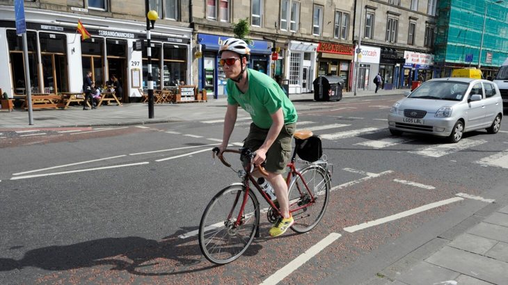Man cycling on road with car in background