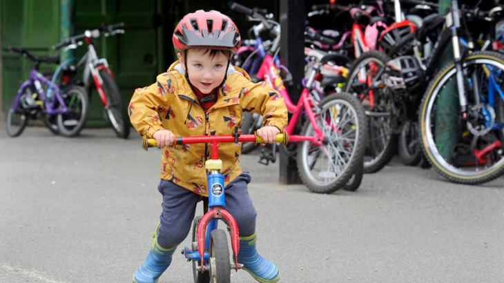 Toddler with helmet and yellow coat on, riding a red bicycle