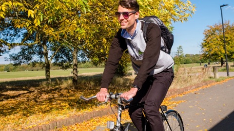 A young man cycles along a cycle route on a sunny autumnal day 