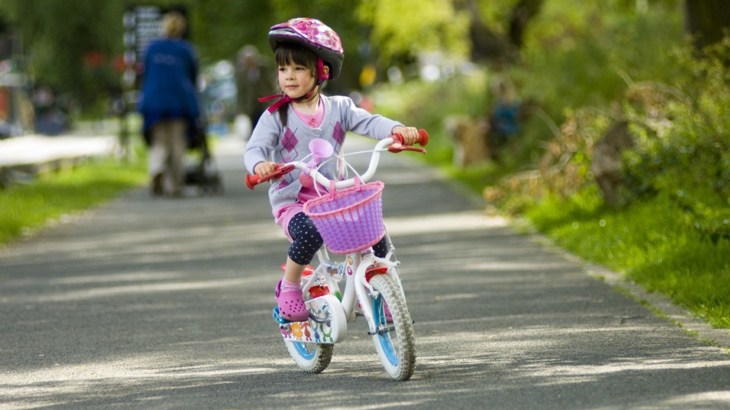 Toddler riding a pink bike on a path through a park 
