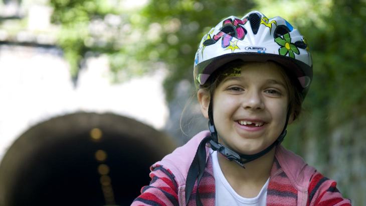 Close up of a child smiling wearing a helmet on a traffic-free National Cycle Network route
