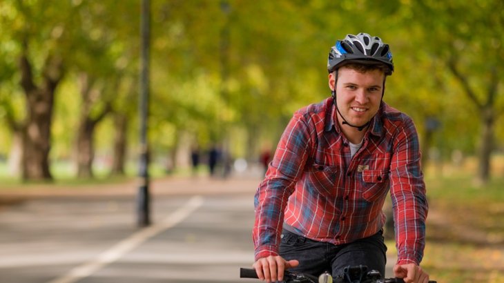 Man in red shirt and cycling helmet riding on cycle path through wooded park