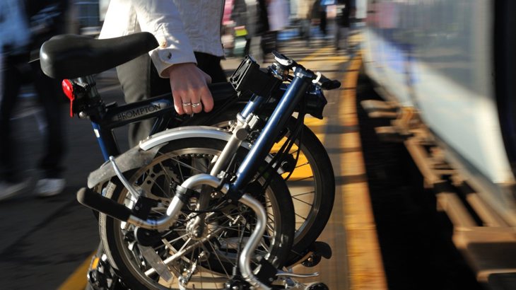 A person in white jacket carrying Brompton bike onto a train