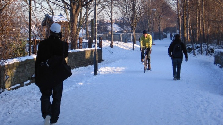 A cyclists rides through the snow on a shared path with walkers