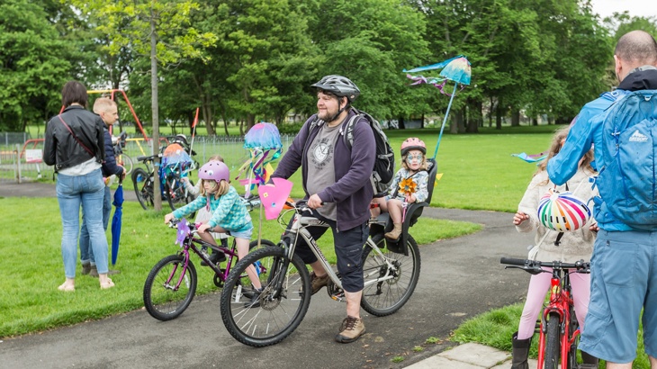 Dad with daughter in bike seat and other child on own bike next to him