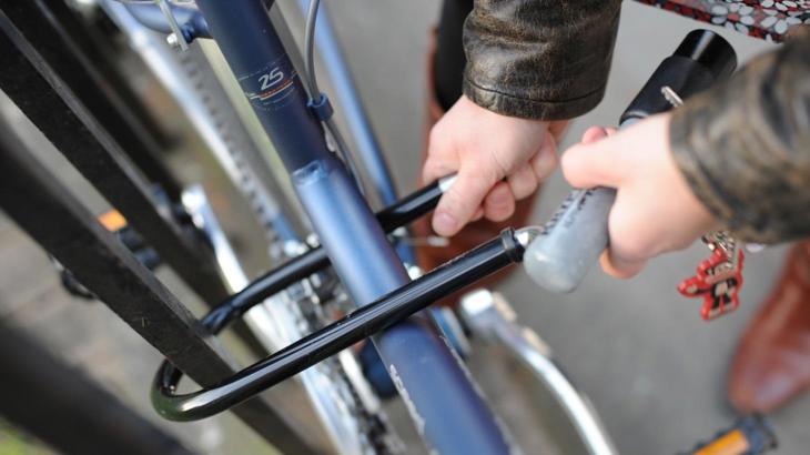 Person's hands locking blue bike frame to black railings using black D-lock
