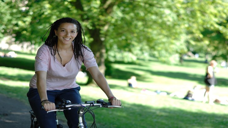 Lady smiling riding her bike through sunny park 