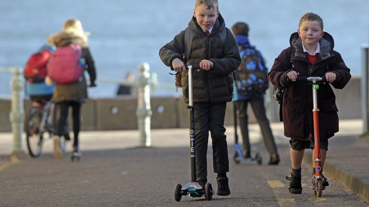 Two schoolboys in black coats on scooters ©2018, Neil Hanna