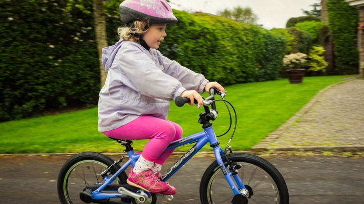 Little girl in pink helmet cycling past on a blue bicycle