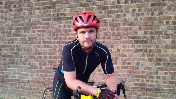 Man in black cycling top and red cycling helmet leaning on road bike handlebars 