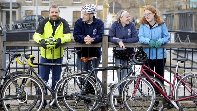 A group of colleagues, two male and two female, posing near a canal with their bicycles