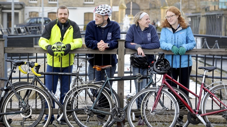 A group of colleagues, two male and two female, posing near a canal with their bicycles