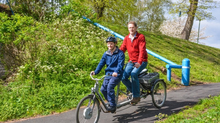 Man with Down Syndrome and older man riding tandem tricycle on traffic-free path