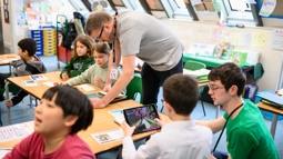 Two Walk Wheel Cycle Trust staff members look at iPads at school desks alongside children using Minecraft to explore engineering