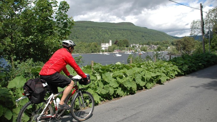 Cycle tourer on a road beside river and mountains