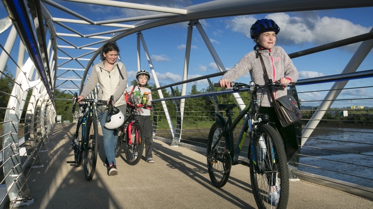 Family walking with bicycles over a bridge