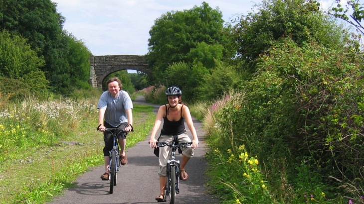Man and woman cycling on greenway with bridge in the background
