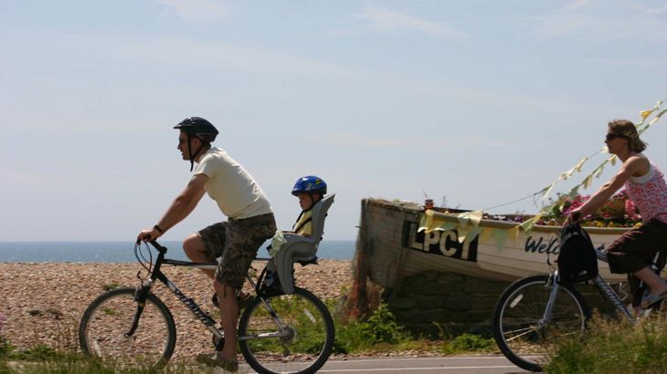 Cyclist with young child in bike seat with woman cyclist behind on coastal route