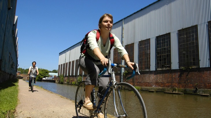 Two cyclists on canal towpath in industrial area
