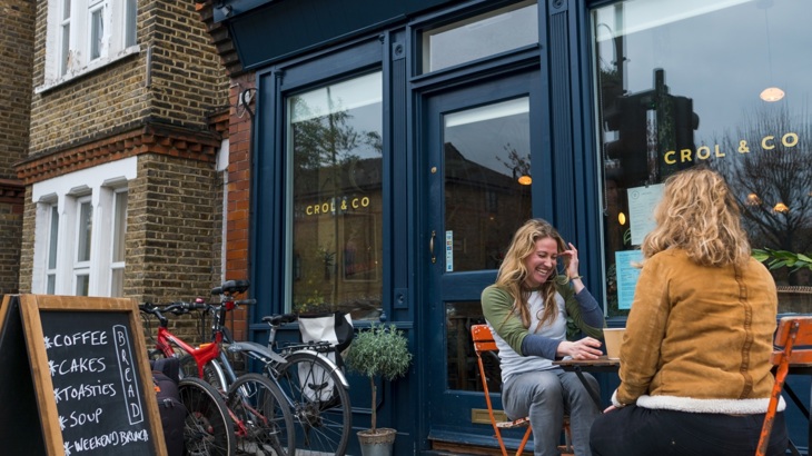 Two people chatting over coffee outside cafe with bikes