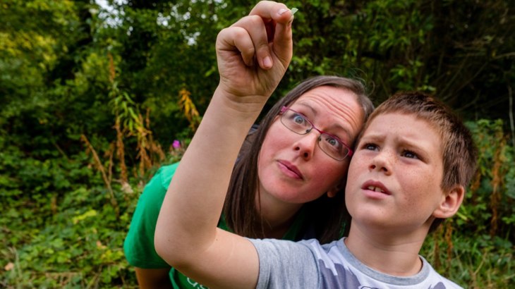 Woman in green t shirt and boy in grey t shirt inspecting something small that the boy is holding
