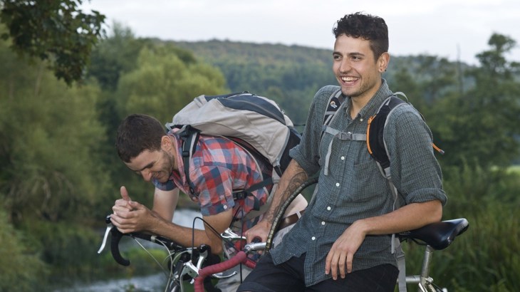 Two men wearing backpacks, resting on their bikes
