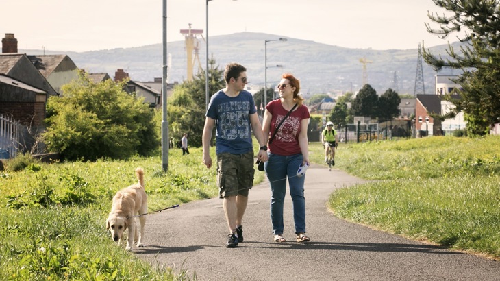 Man and woman holding hands and walking dog on path in suburban area