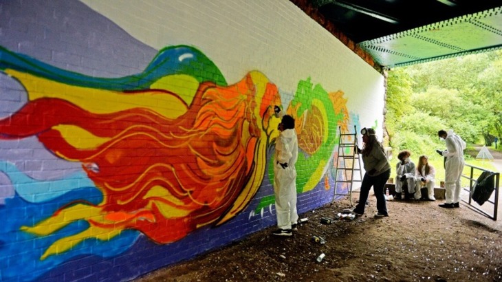 Teenagers painting a dragon mural under a bridge