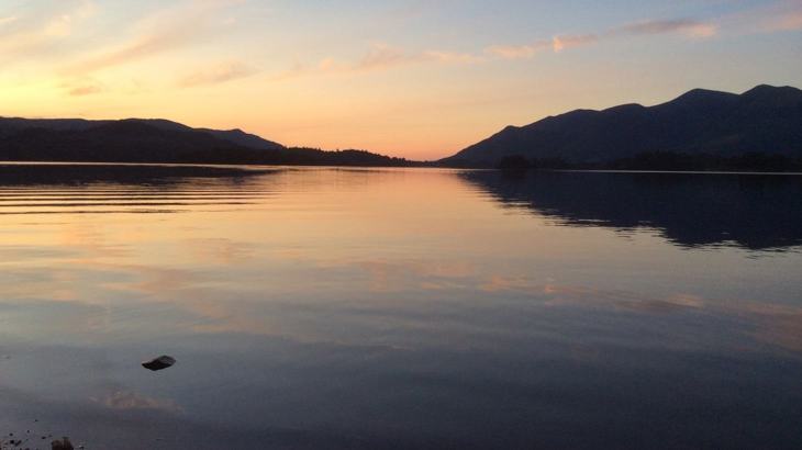 View of flat-calm lake reflecting pink and blue sky and hills