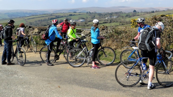 Eight cyclists on country road overlooking green hills in Devon