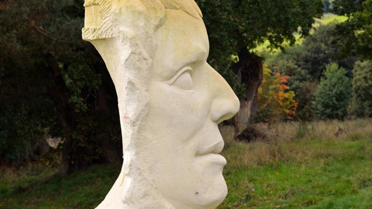 White stone sculpture of a face with grass and trees in the background