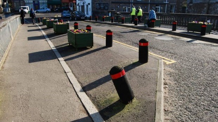 Black bollards with red stripes on pavement by road