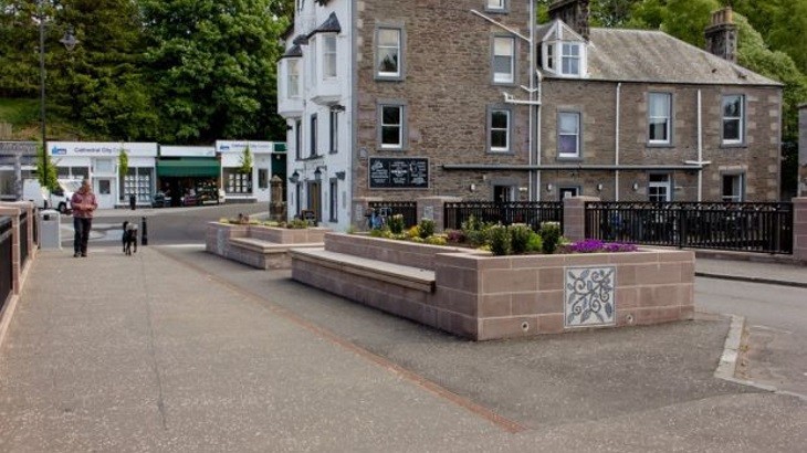 Bridge in town with pavement, road, pub building and dog walker