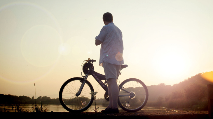 A person with their gravel bike standing in front of Loch Leven to watch the sunset.