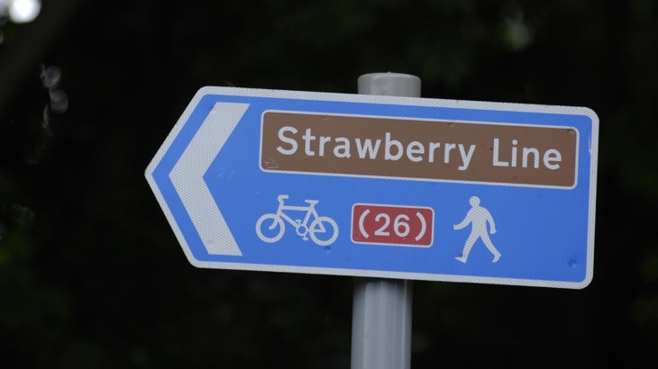 Blue directional sign on pole with bracketed number 26, picture of bike and walker, and title "Strawberry Line"