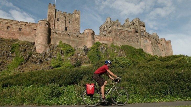 Cyclist with helmet and panniers cycling passing brown brick castle