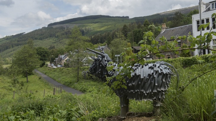 A Metal Sculpture Of A Cow On A Cycle Path 