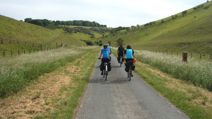 Group of touring cyclists on tarmac path through grassy valley