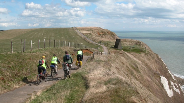 Group of touring cyclists on tarmac path  on cliff with white chalk to the side