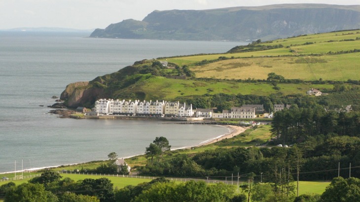 View of coastal village with row of white buildings, plus fields and trees