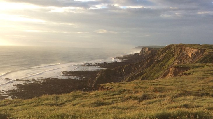 Grass-covered cliffs with sea and sun shining through the clouds