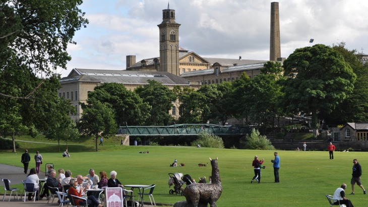 Old industrial building with green, outdoor cafe seating area and metal sculpture of a lama 