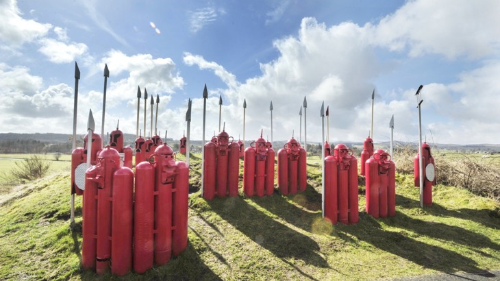 Red and grey metal sculptures shaped like Roman legionnaires with spears