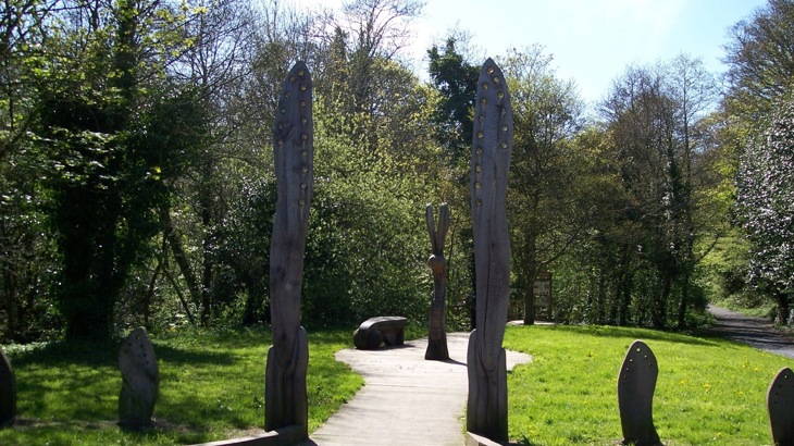 Upright wooden artworks shaped like dragonfly wings on path leading into woodland park