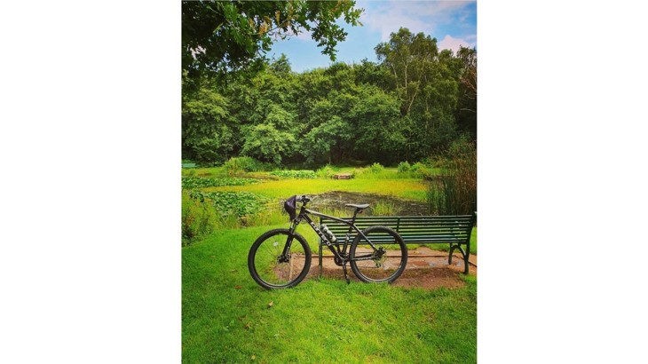 Bike with peaked cap on handle bar leaning up against park bench overlooking pond