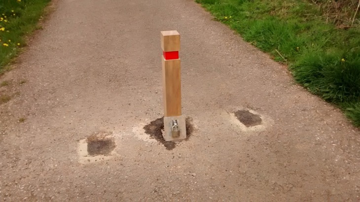 Removable timber bollard with a reflective band, set in the centre of a traffic-free path with grass to either side.
