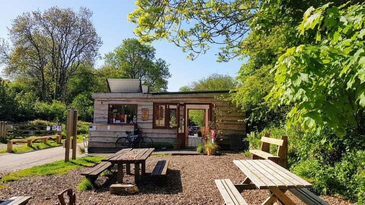 Wooden cafe building with wooden benches out the front and trees to the side